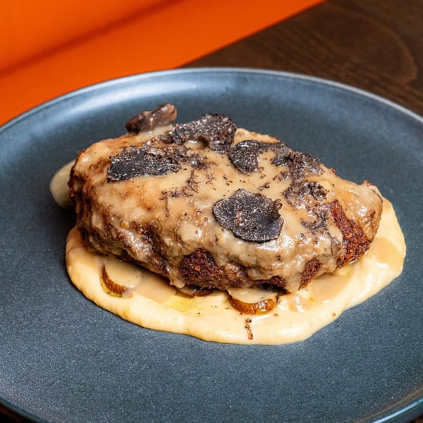Chicken fried steak with gravy and black truffle shavings on a dark plate.