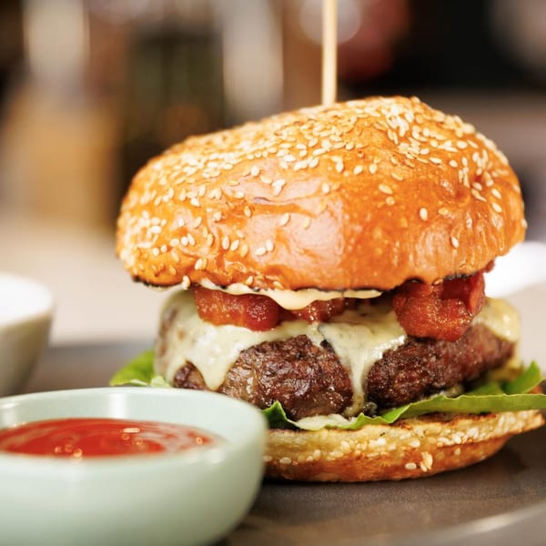 A juicy cheeseburger with bacon, lettuce, and a sesame seed bun, served with ketchup.