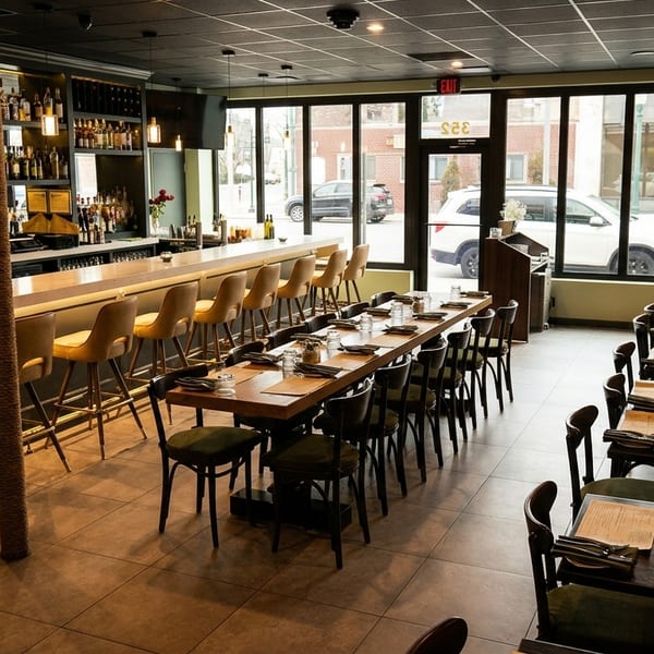 Modern restaurant interior with a long bar, high stools, and dining tables with banquette seating.