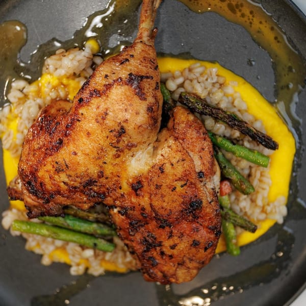 Crispy roasted chicken with asparagus and barley on a yellow puree, served on a dark plate.