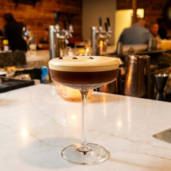 Espresso martini with coffee beans on top, on a white marble bar with blurred patrons.