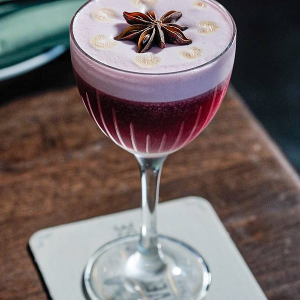 A vibrant red cocktail with a foamy top and a star anise garnish on a branded coaster.
