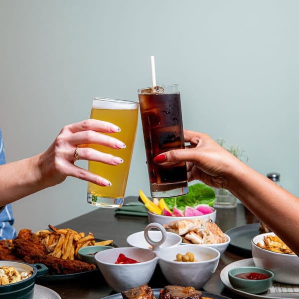 Two people toasting drinks over a table laden with various dishes, including short ribs and fries.