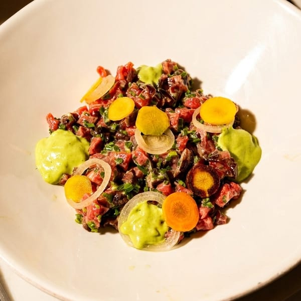 Beef tartare with avocado puree, sliced carrots, and onions on a white plate.